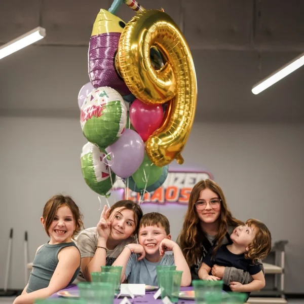 Group of happy kids sitting at a set birthday party table with balloons